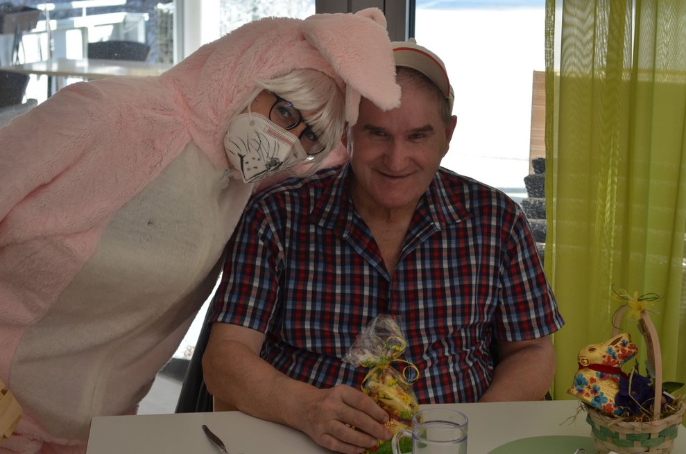 Eine Person, die als Osterhase verkleidet ist, steht neben einem Bewohner.