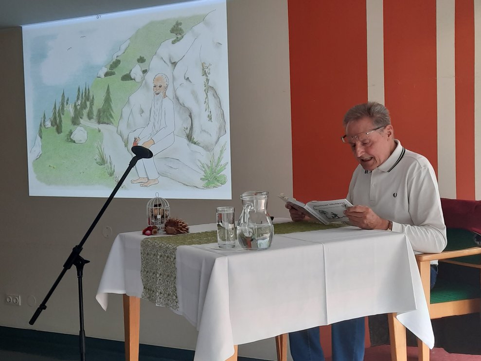 Herr Krammer sitzt bei Tisch und liest aus seinem Buch.