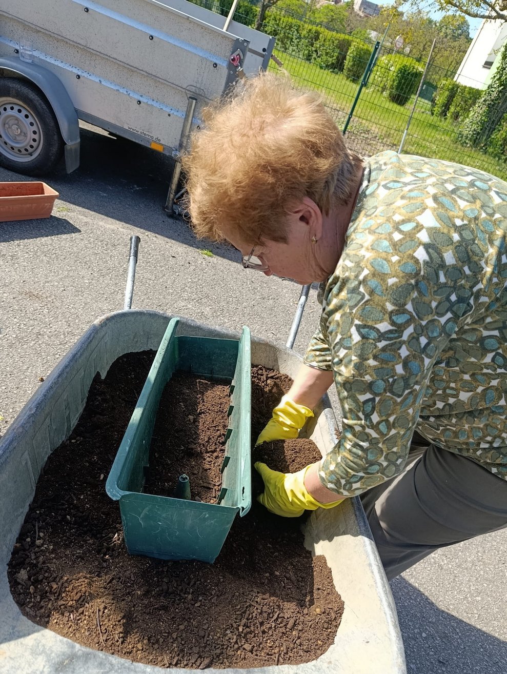 Ehrenamtlich Tätige befüllt Blumenkisterl mit Erde.