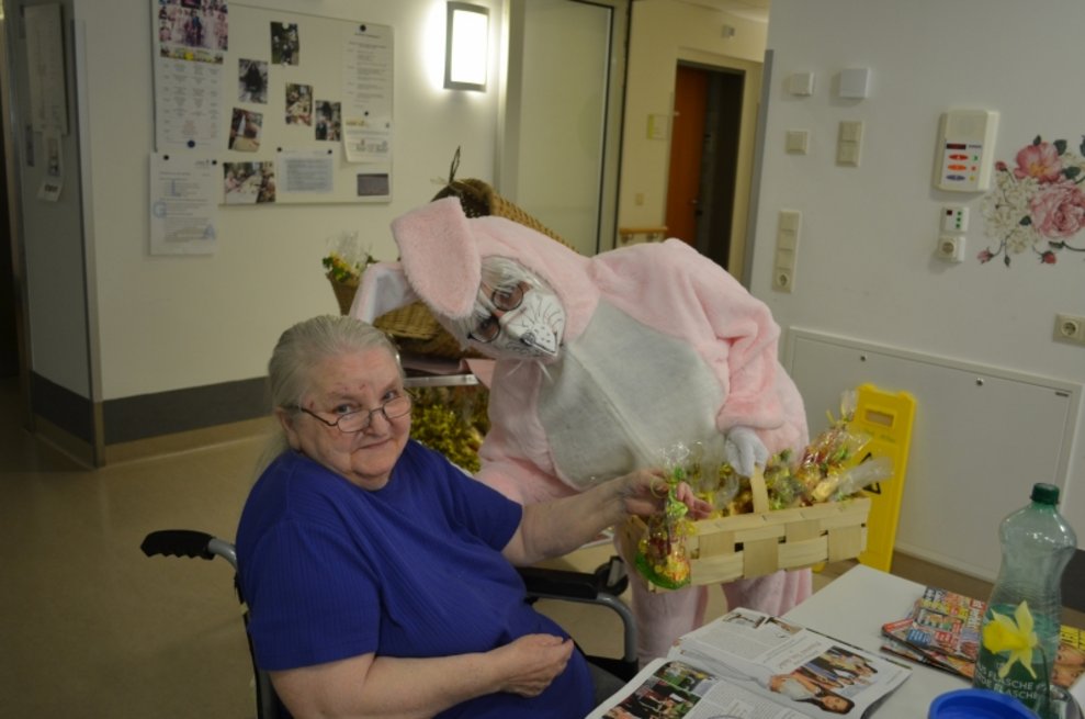 Eine Person, die als Osterhase verkleidet ist, bringt einer Bewohnerin einen Geschenkkorb.