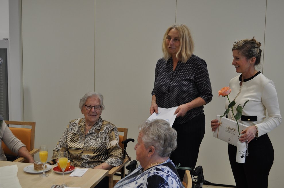 zwei Frauen gratulieren einer älteren Dame bei der Geburtstagsfeier