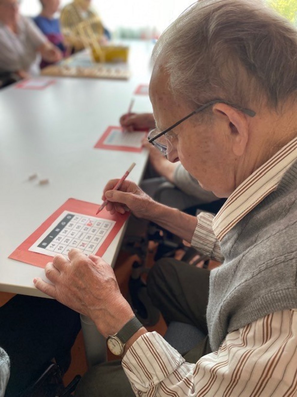 Bewohner sitzt beim Tisch und macht ein Kreuz bei einer Zahl