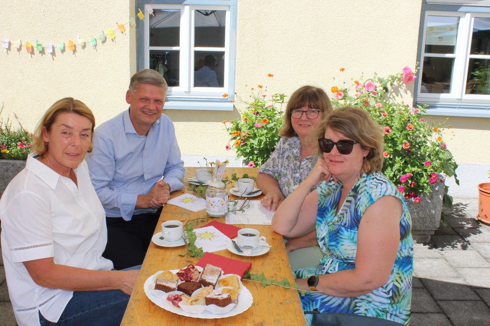 Vier Personen sitzen mit Kaffee und Kuchen am Tisch beisammen