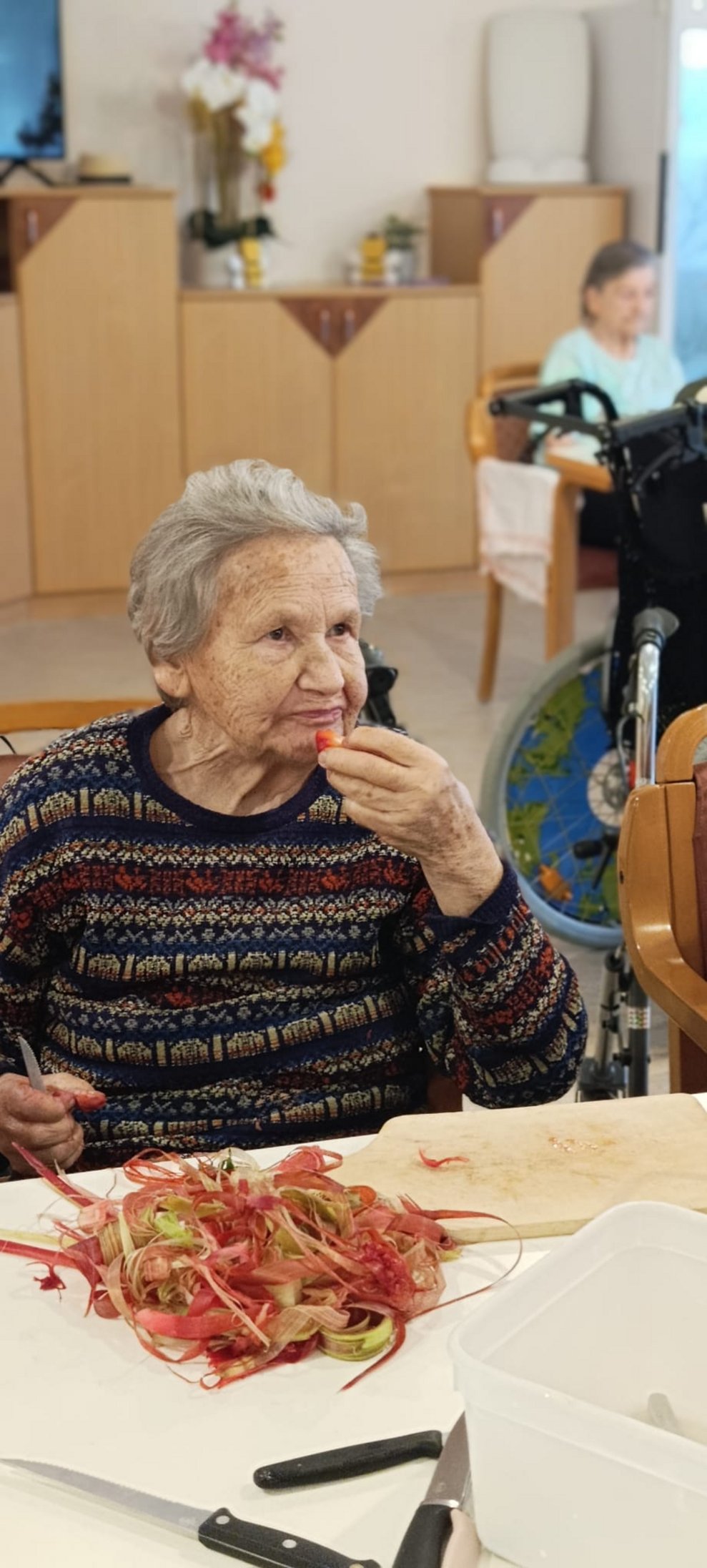 Bewohnerin isst eine Erdbeere. Etliche Schalen von Rhabarber liegen auf Tisch.