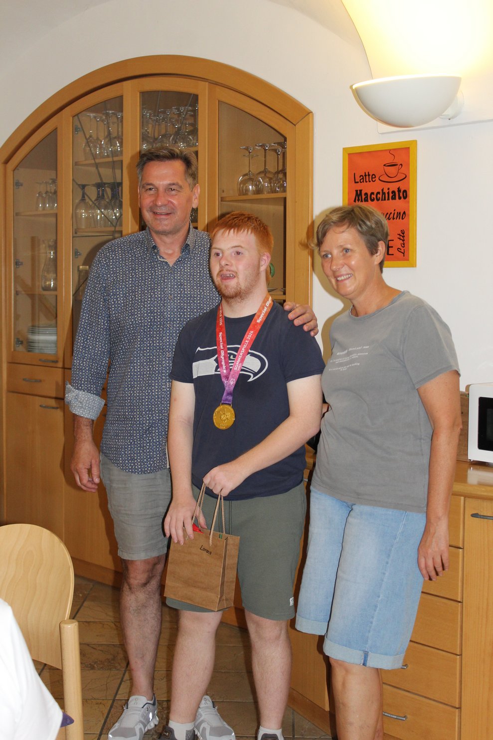 Drei Personen stehen nebeneinander und der in der Mitte hat eine Medaille umgehängt.