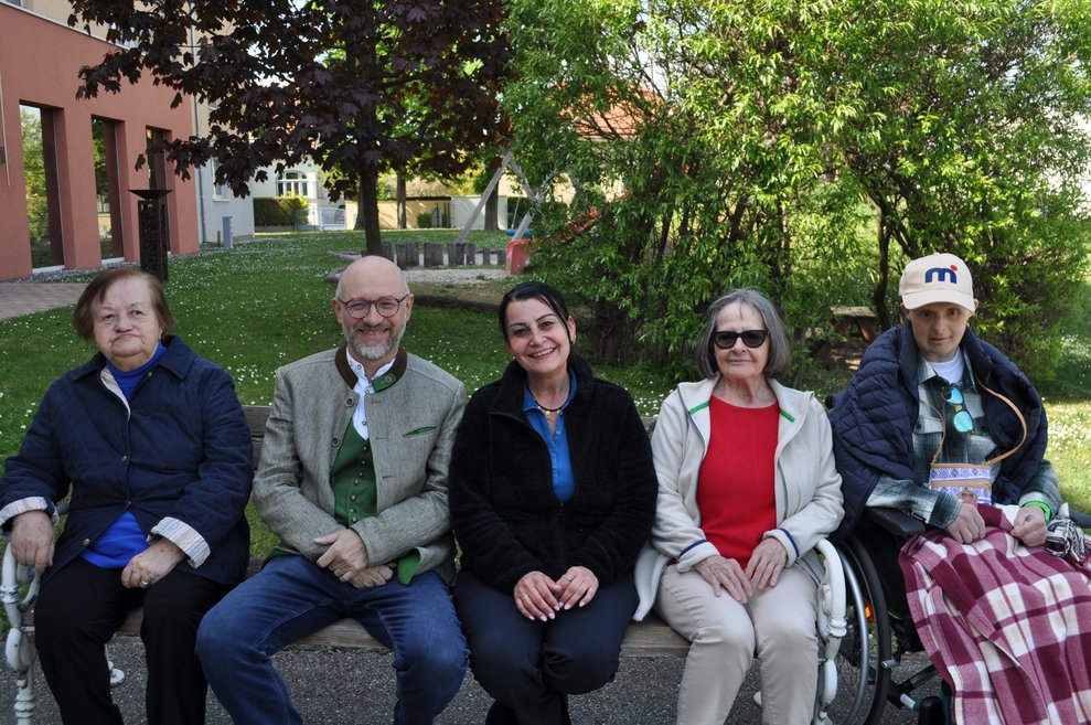 Fünf Personen sitzen im Garten auf einer Bank