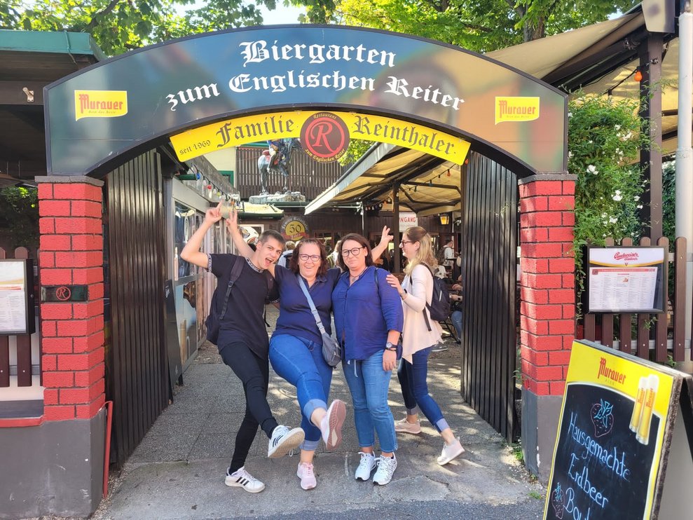 Drei Personen unter dem Schild vom Biergarten.