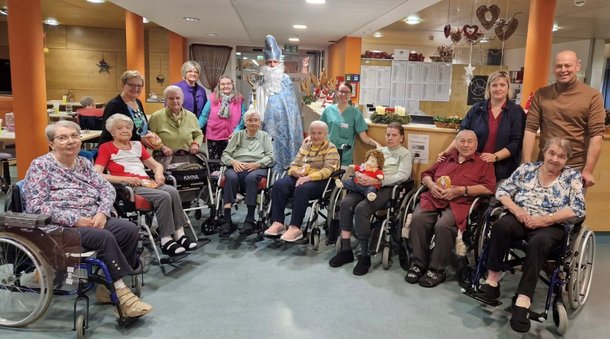 Gruppenfoto von Bewohnerinnen und Bewohner mit Mitarbeiterinnen und Mitarbeiter im Hintergrund steht der Nikolaus mit einem hellblauen Umhang 