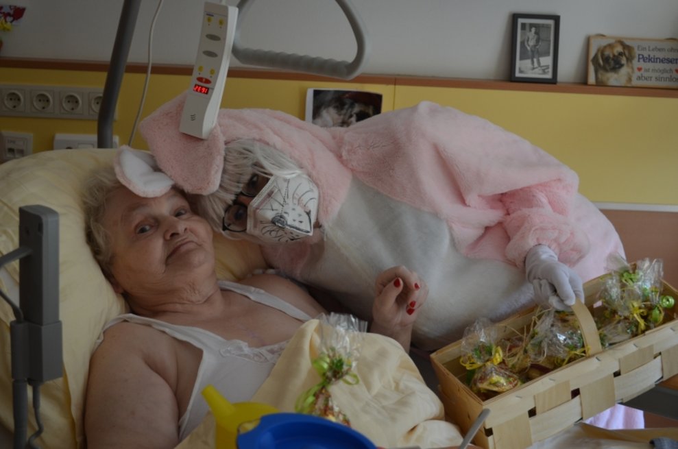 Eine Person, die als Osterhase verkleidet ist, steht neben einer Bewohnerin, die im Bett liegt.