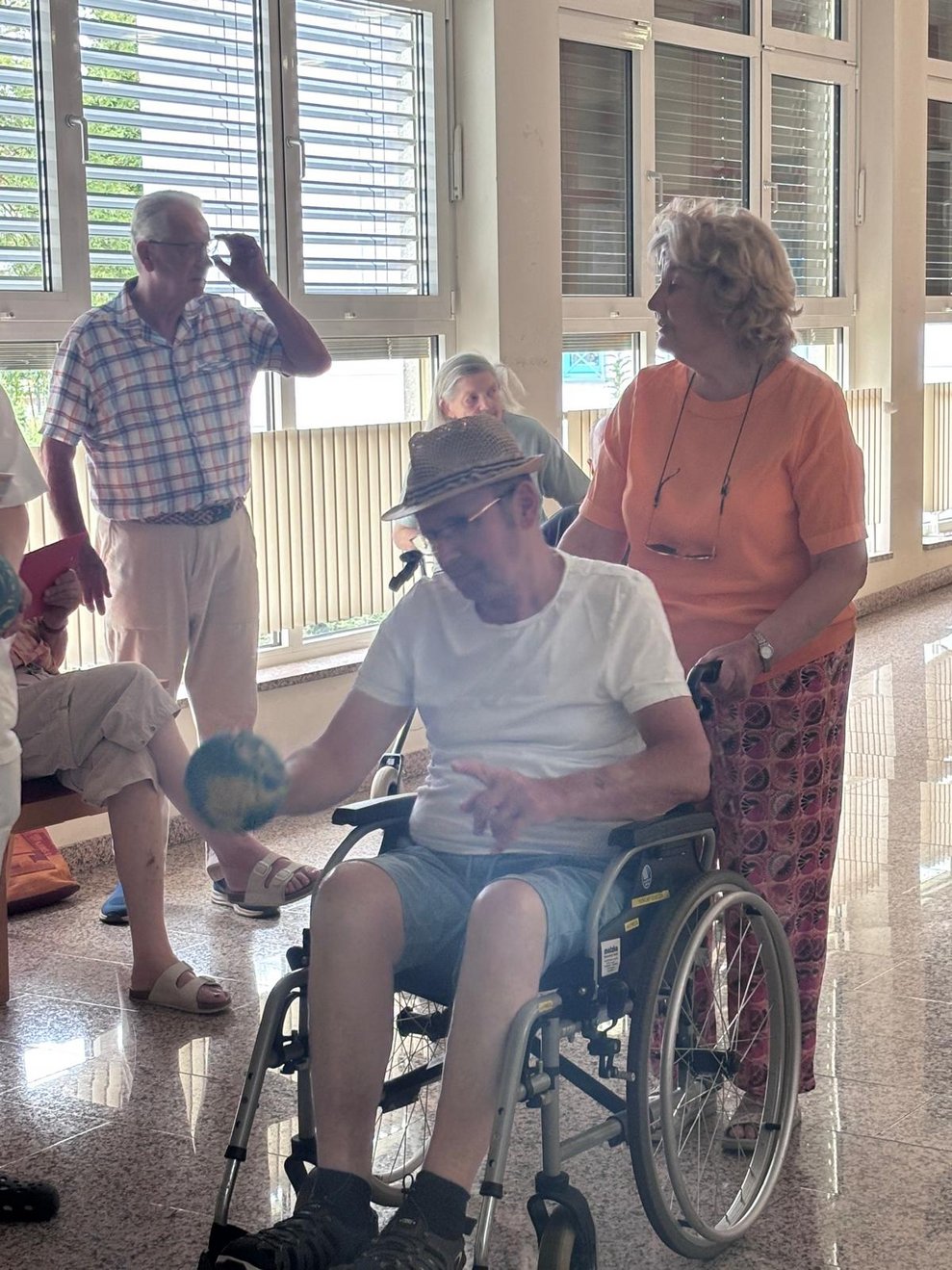 Bewohnerin im Rollstuhl hält Kegelball in den Händen. Ehrenamtlich Tätige hält Rollstuhl mit Bewohnerin.