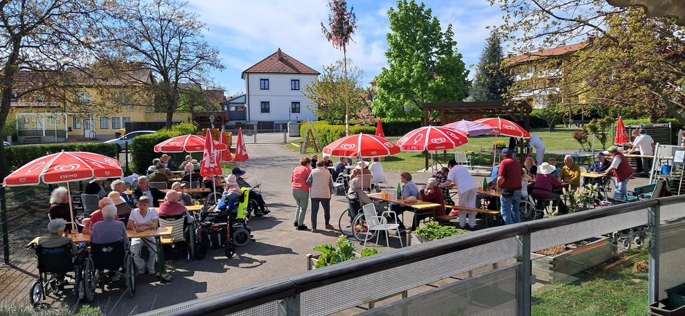 Viele Personen im Garten. Sonnenschirme, Tische und Bänke sind aufgestellt.