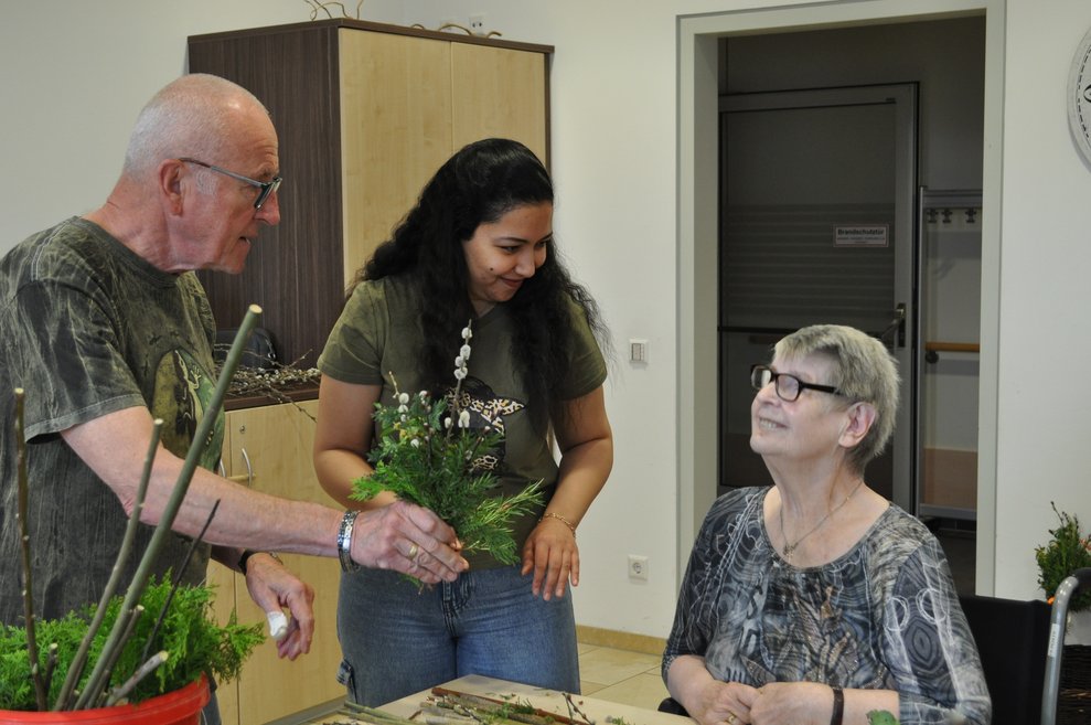 Ein Herr und eine junge Frau überreichen einer älteren Dame einen Palmbuschen 