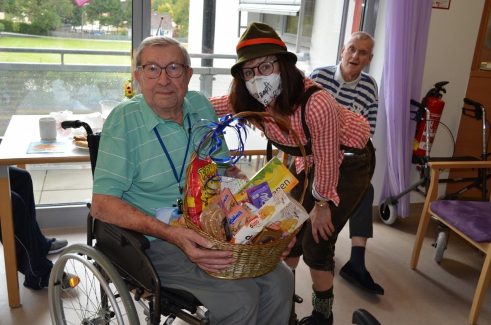 Ein Bewohner hält einen Geschenkkorb und eine Betreuerin steht neben ihm.