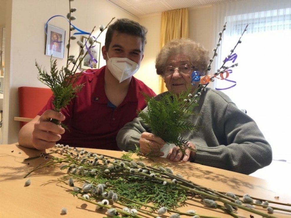 Ein Betreuer und eine Bewohnerin halten Palmbesen.