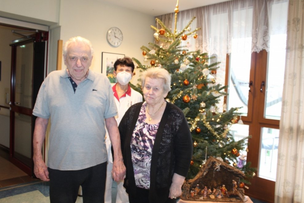 Eine Betreuerin, eine Bewohnerin und ein Bewohner stehen beim Christbaum.