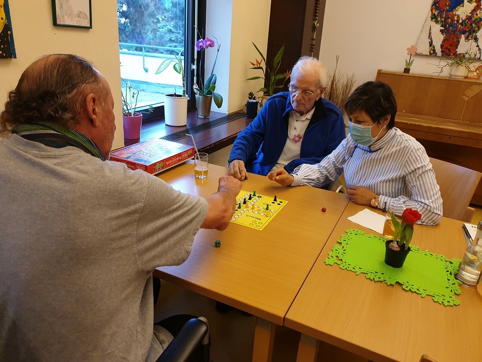 Bewohner und eine Betreuerin spielen "Mensch ärger dich nicht".