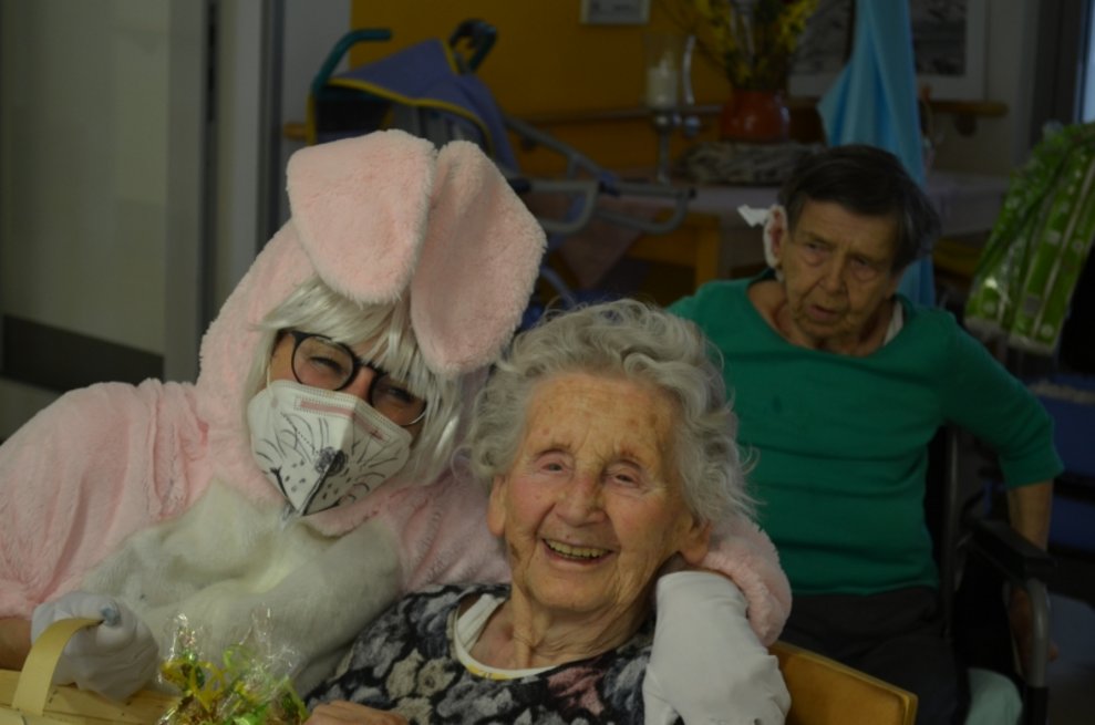 Eine Person, die als Osterhase verkleidet ist, steht neben einer Bewohnerin.