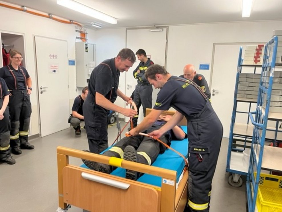 Ein Feuerwehrmann wird von seinen KollegInnen im Bett gesichert.