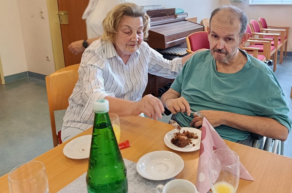 Ehrenamtlich Tätige hilft Bewohner mit dem Tortenstück.