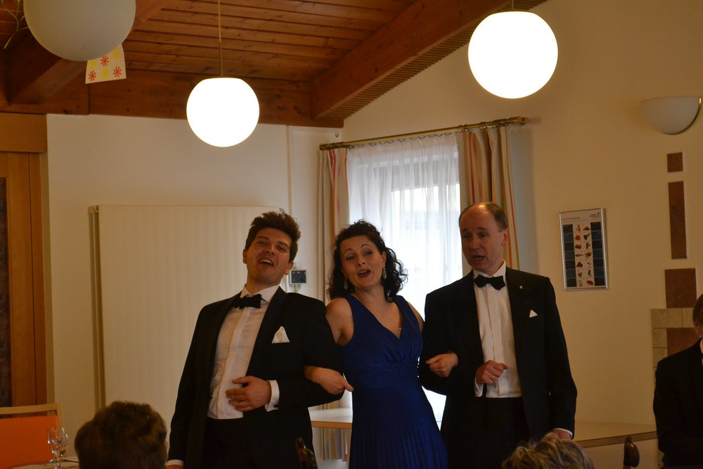 Zwei Männer und eine Dame sind festlich gekleidet, singen gemeinsam