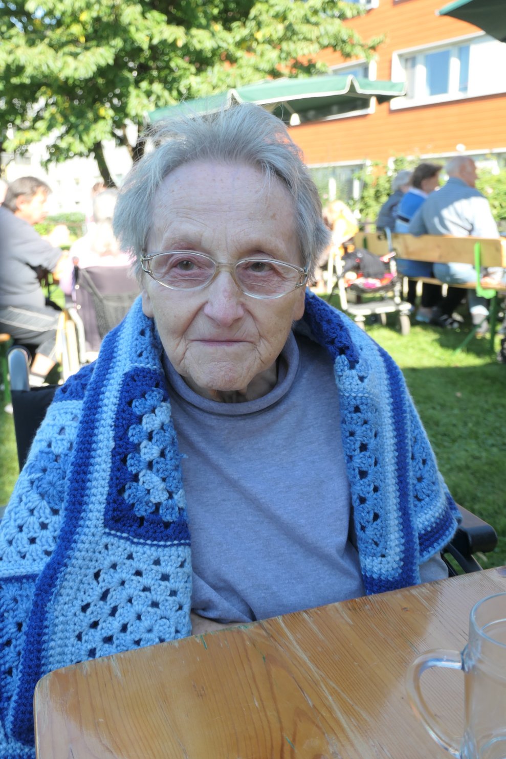 Eine Frau mit Wolldecke sitzt auf der Heurigengarnitur.