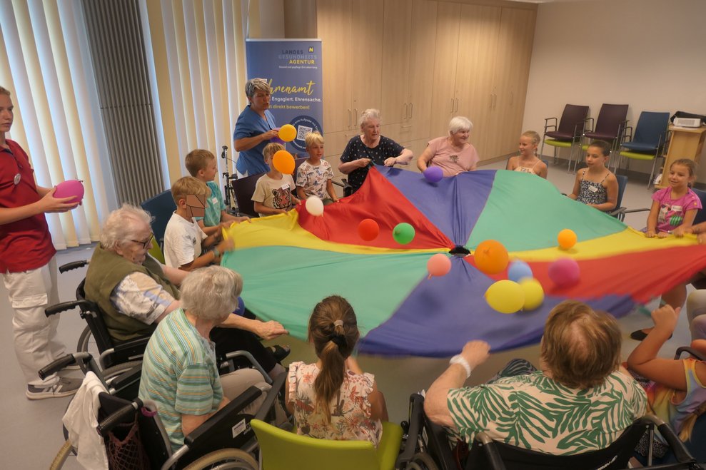 Die Kinder und SeniorInnen spielen mit dem Fallschirm und Luftballon.