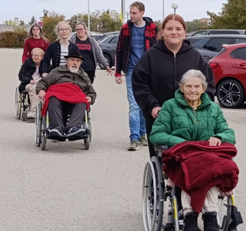 Schülerinnen schieben Rollstühle mit BewohnerInnen. Alltagsbegleiter und eine Schülerin gehen daneben.