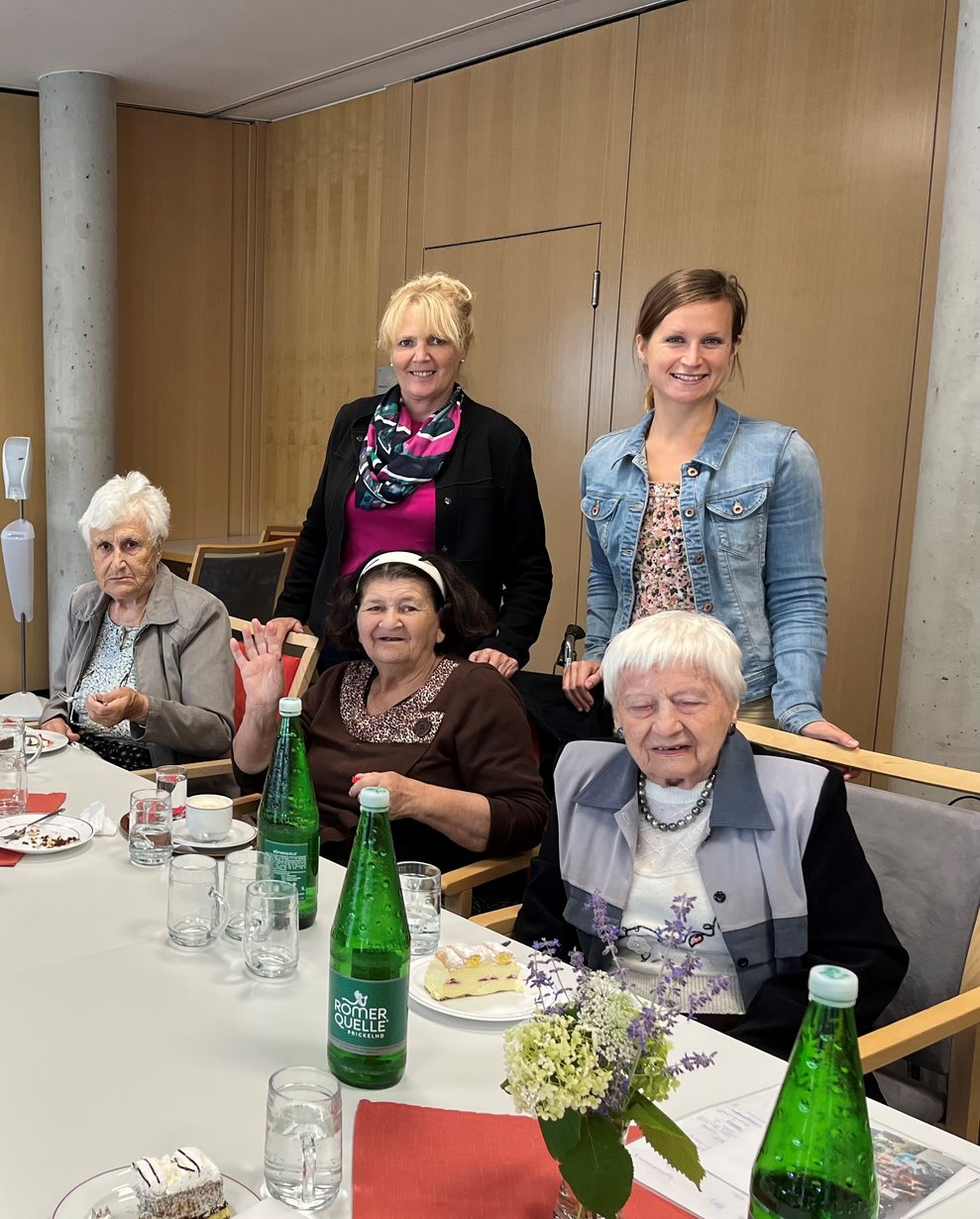 Bewohnerinnen beim Tisch mit zwei Damen stehend im Hintergrund