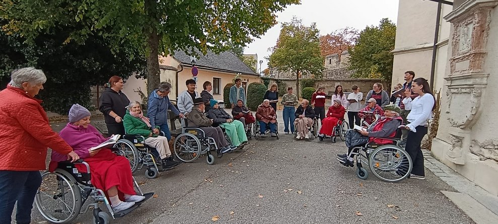 BewohnerInnen, SchülerInnen, Lehrer und ehrenamtlich Tätige singen vor Kirche.
