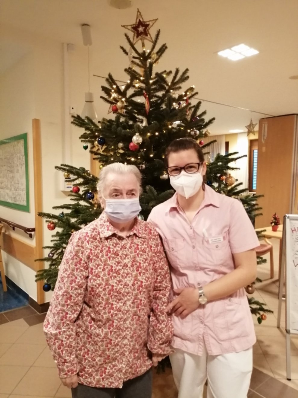 Eine Bewohnerin und eine Betreuerin stehen beim Christbaum.