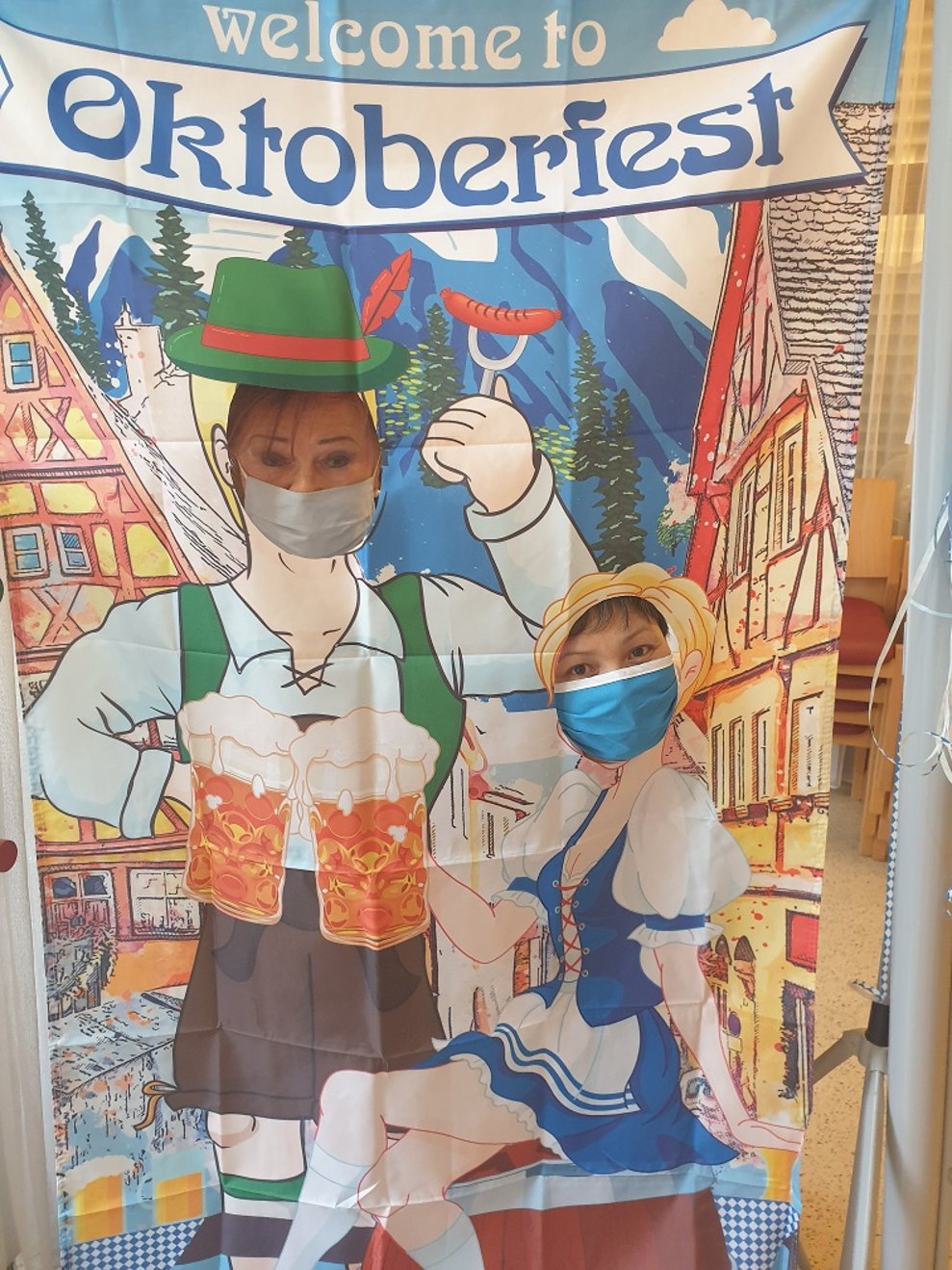 Zwei MitarbeiterInnen schauen durch einen Oktoberfest-Aufsteller durch.