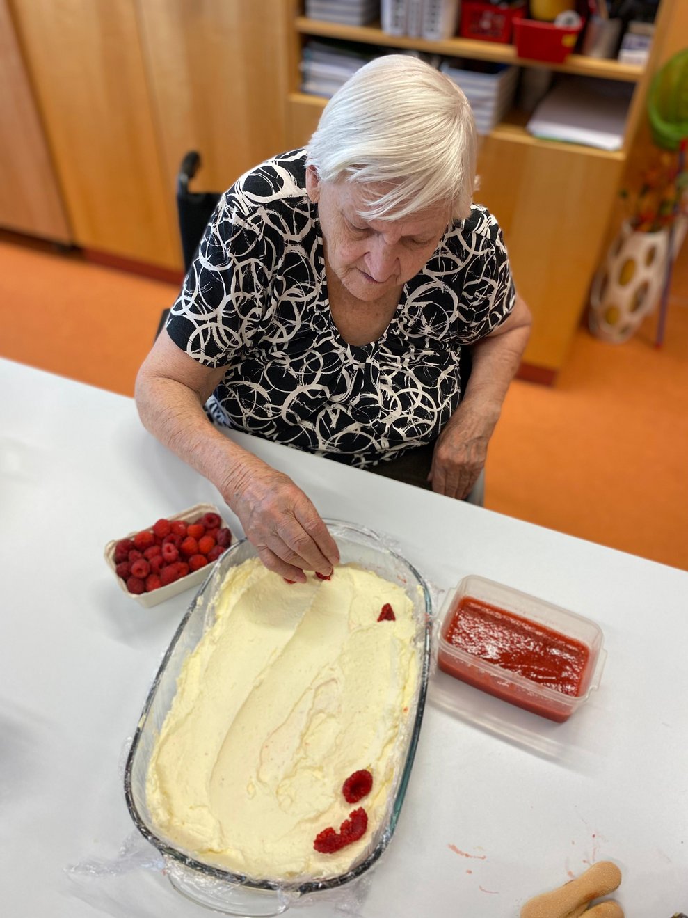 Eine Dame legt Himbeeren auf das Tiramisu.