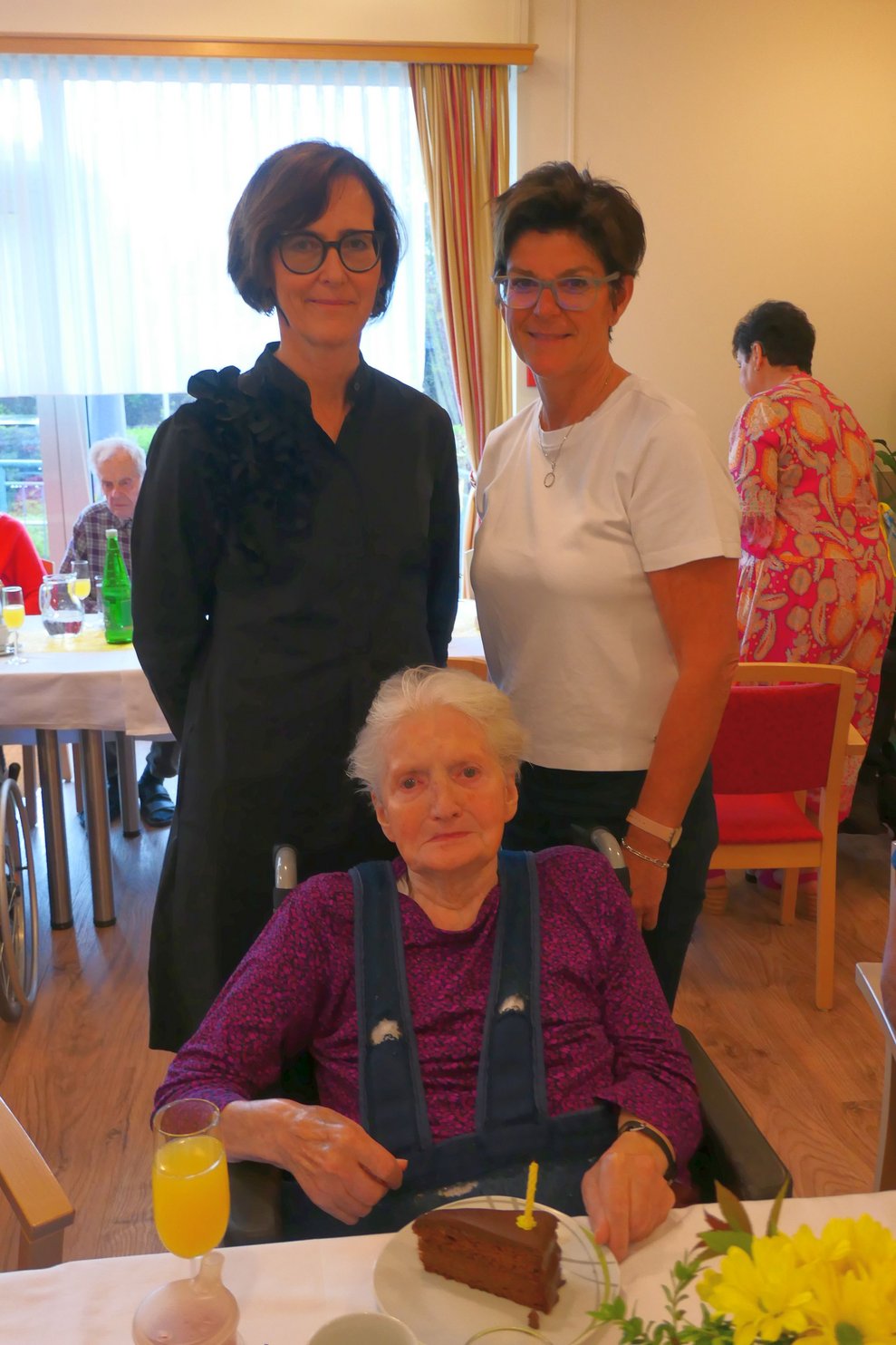 Zwei Damen gratulieren Bewohnerin mit Kuchen.