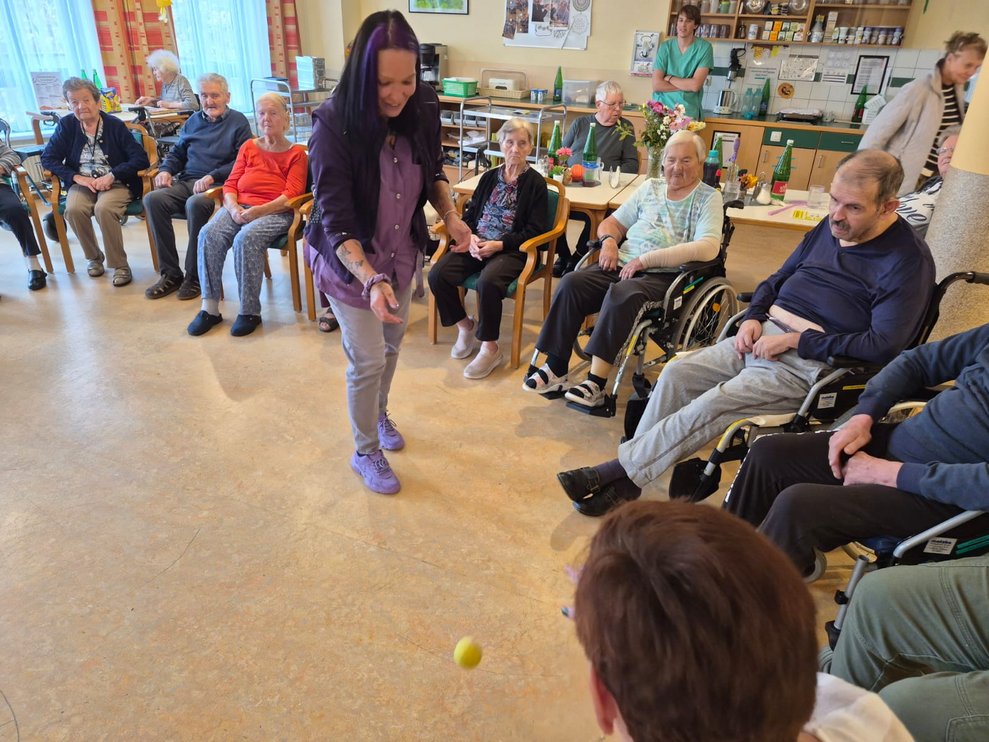 Sitzende BewohnerInnen bei der Bewegungsrunde. Alltagsbegleiterin steht und schaut auf kleinen Ball am Boden.