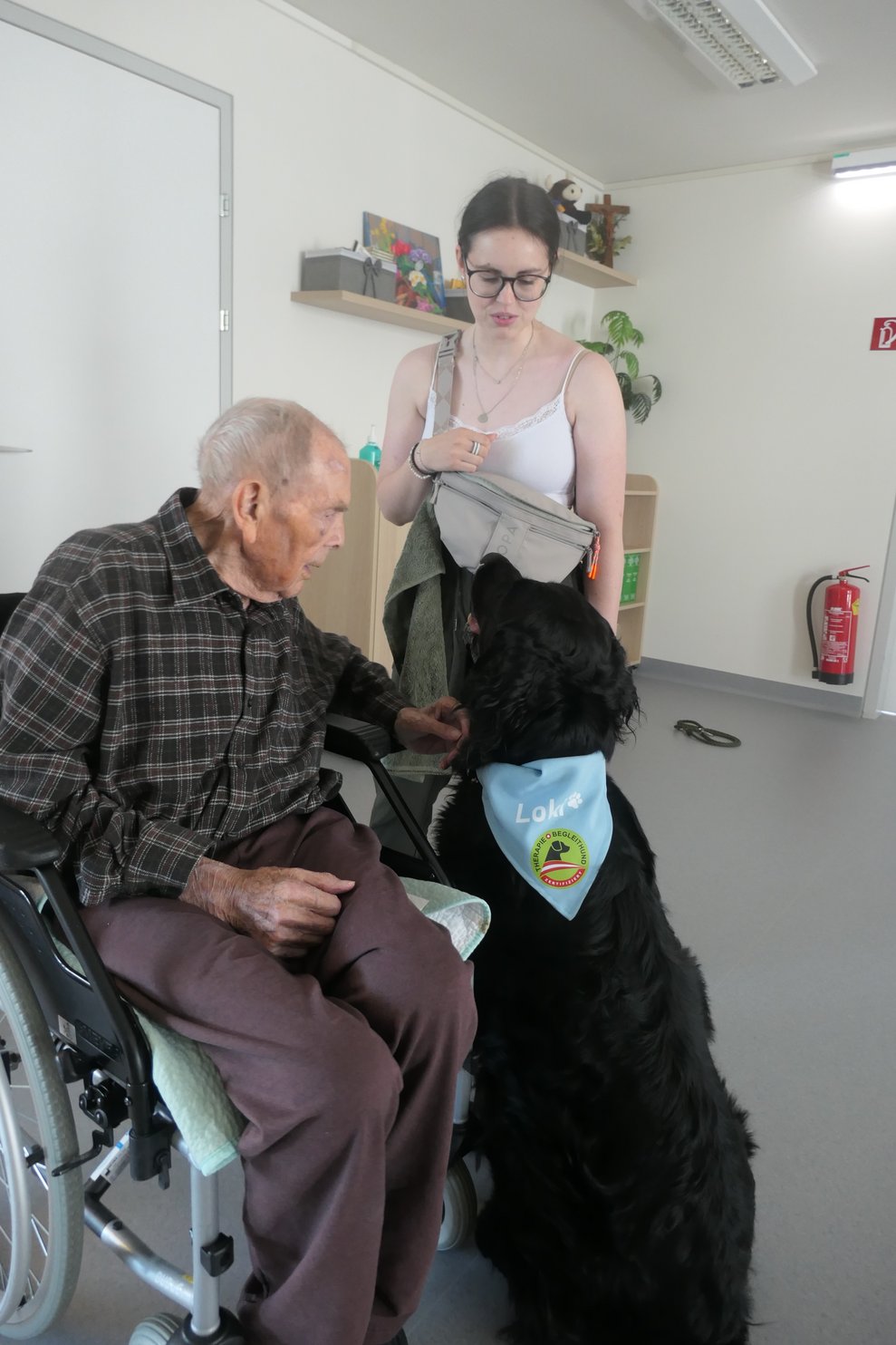 Hund Loki mit Frauchen Carina und einem Herrn im Rollstuhl.