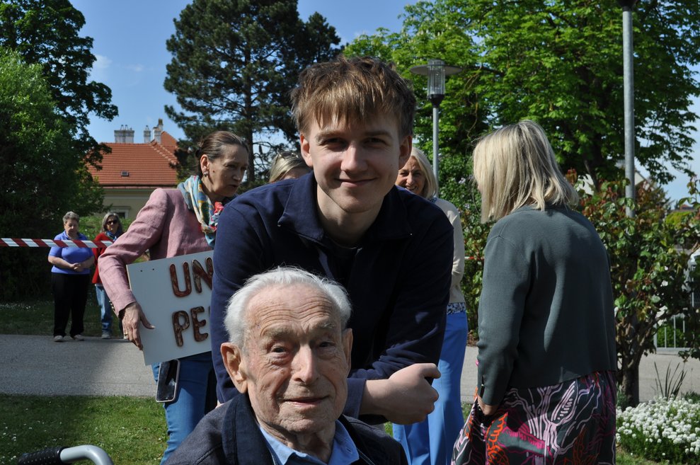 ein älterer Herr und ein junger Mann im Garten vor dem Maibaum