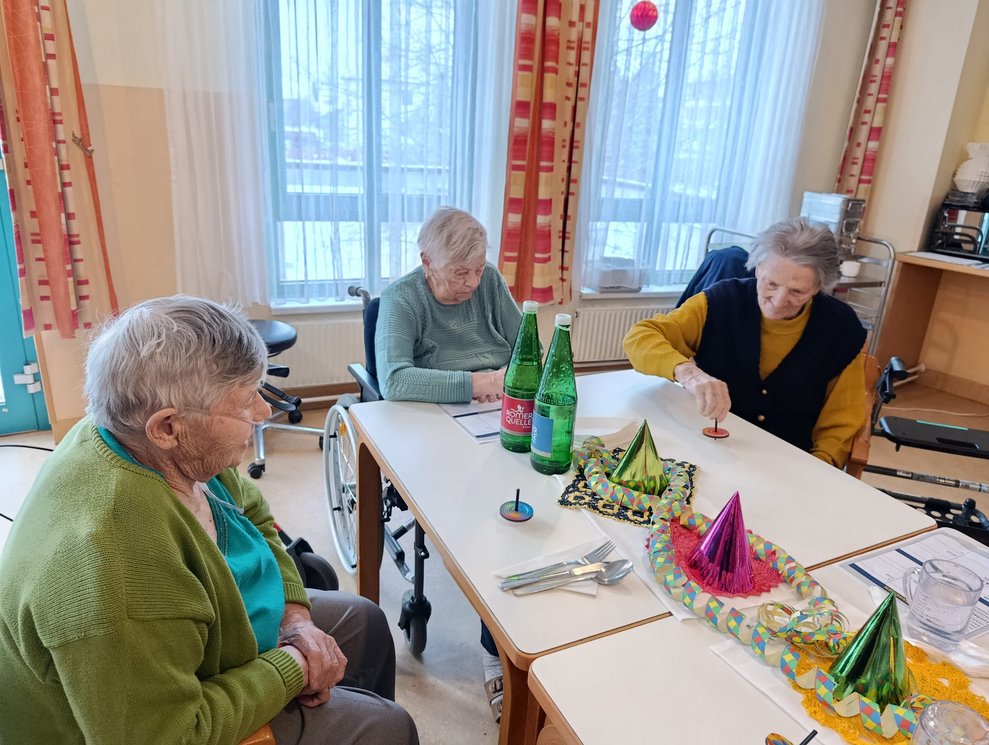 Bewohnerin schaut den tanzenden Kreiseln am Tisch zu. Bewohnerin beim Drehen vom Kreisel am Tisch.