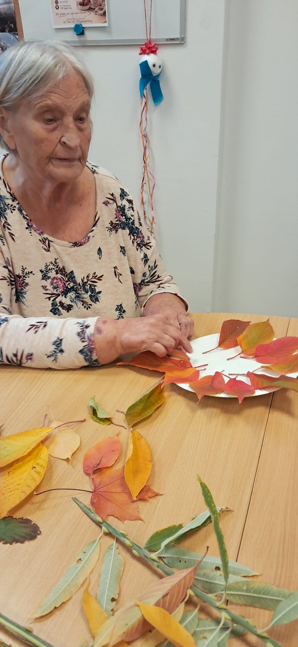 Sitzende Bewohnerin pickt mit Hand bunte Blätter auf den Tellerrand.