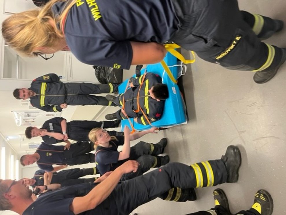 Der Feuerwehrmann wird von zwei Kolleginnen mit der Evakuierungsmatte gezogen.
