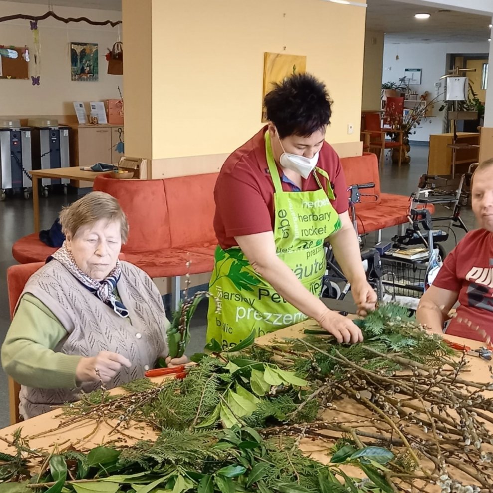 Eine Betreuerin hilft den BewohnerInnen beim Binden der Palmbesen.