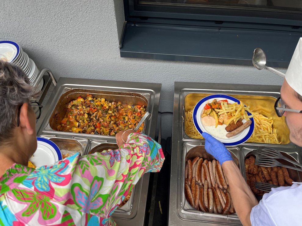 Zwei Mitarbeiter teilen das Essen auf die Teller aus.