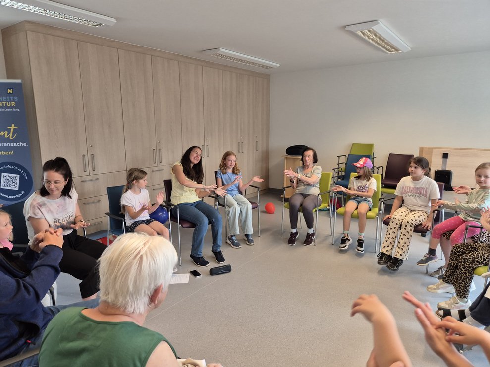 Alle Personen sitzen im Kreis und machen einen Sitztanz.