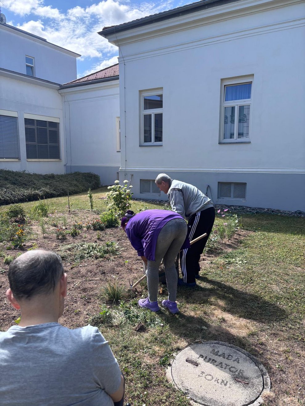 Bewohnerin und Alltagsbegleiterin reisen Unkraut beim Blumenbeet im Garten aus.