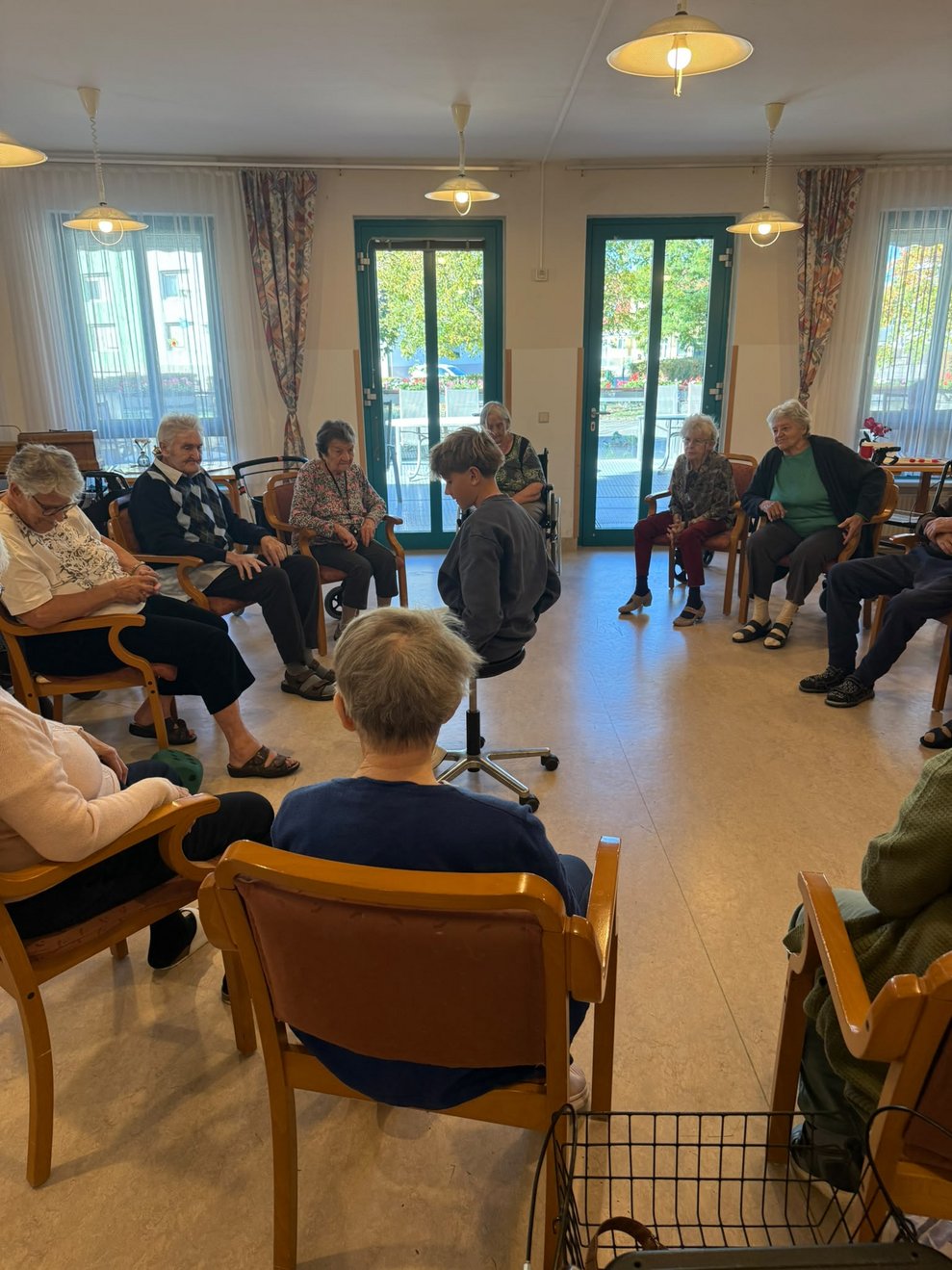 BewohnerInnen sitzen im Kreis. Praktikant sitzt in der Mitte