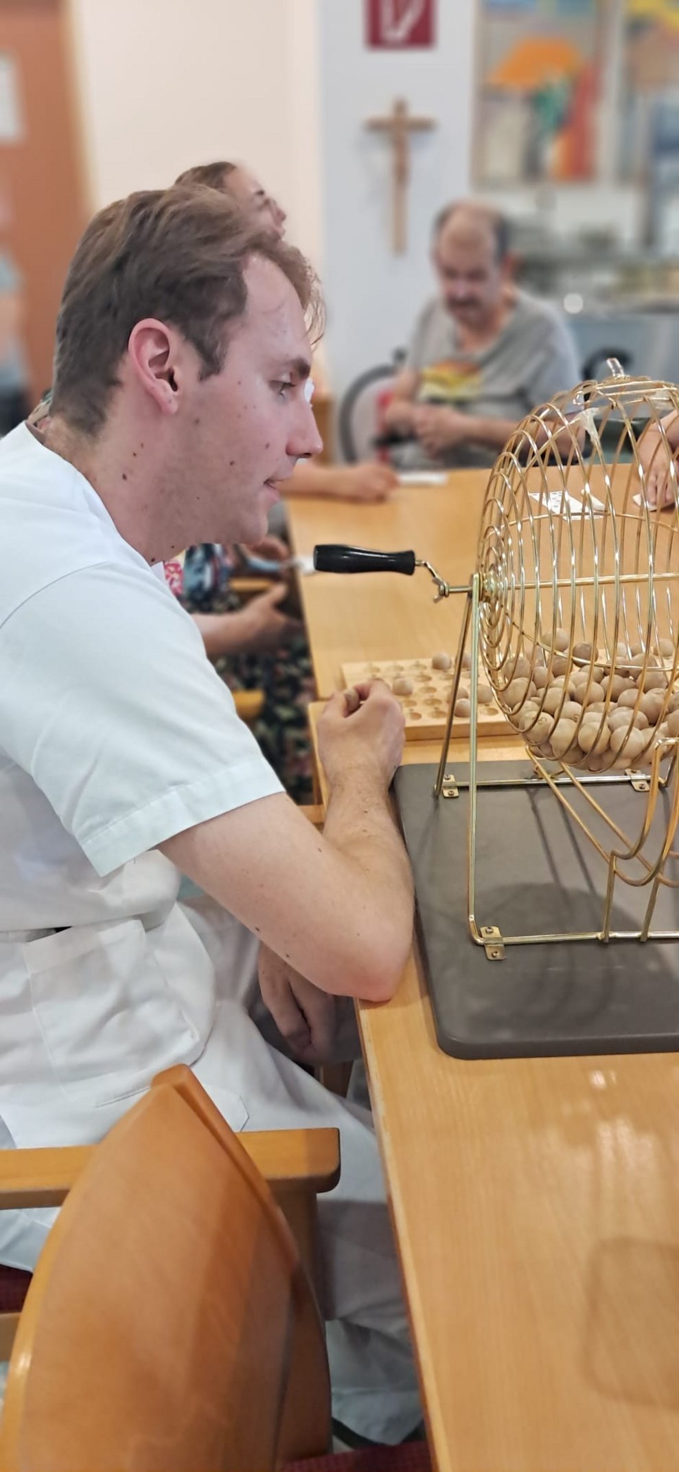 Mann (Aushilfskraft) beim Bingo spielen. Bingorad steht auf Tisch.