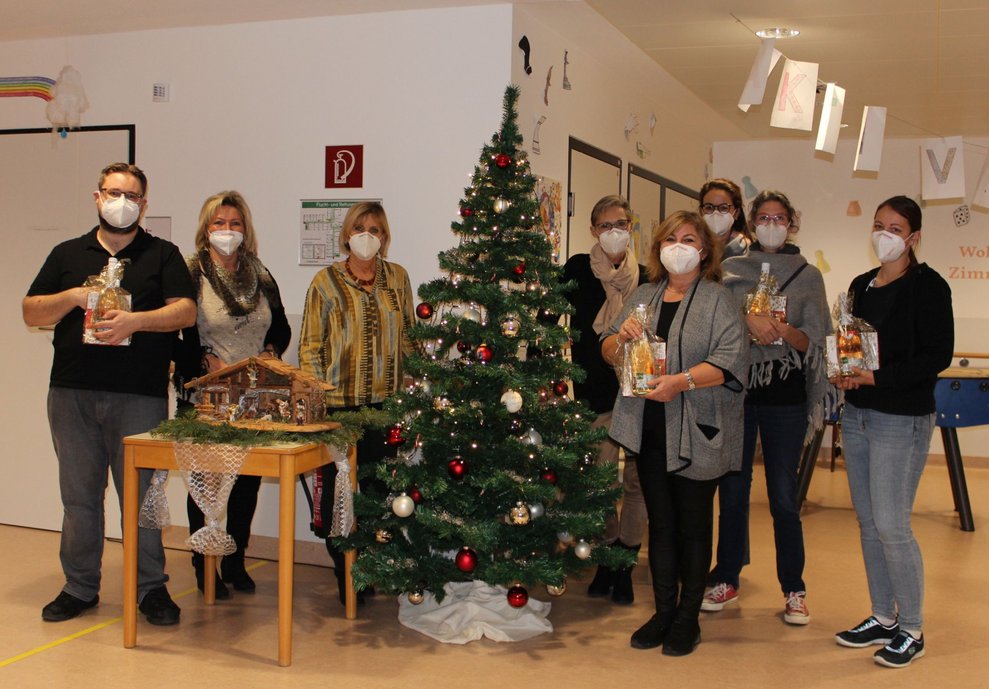 MitarbeiterInnen stehen mit Geschenken vor dem Christbaum.