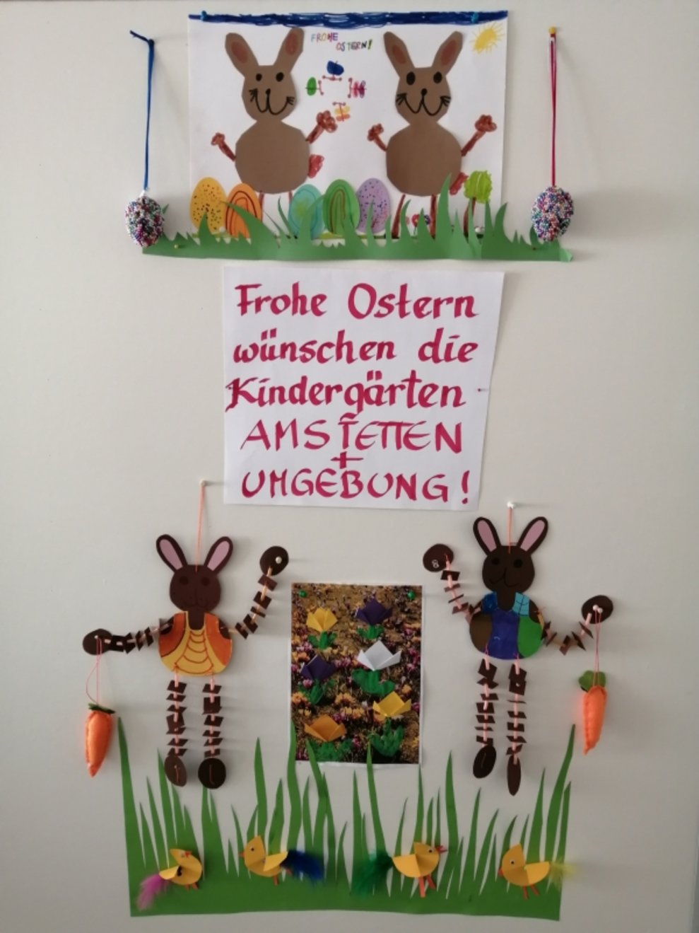 Eine Pinwand mit Hasen und einem Schild, auf dem steht "Frohe Ostern wünschen die Kindergärten Amstetten + Umgebung".