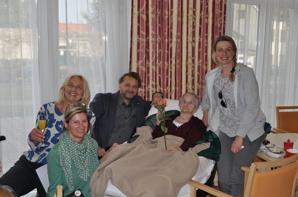mehrere Personen um eine ältere Frau versammelt um zu gratulieren