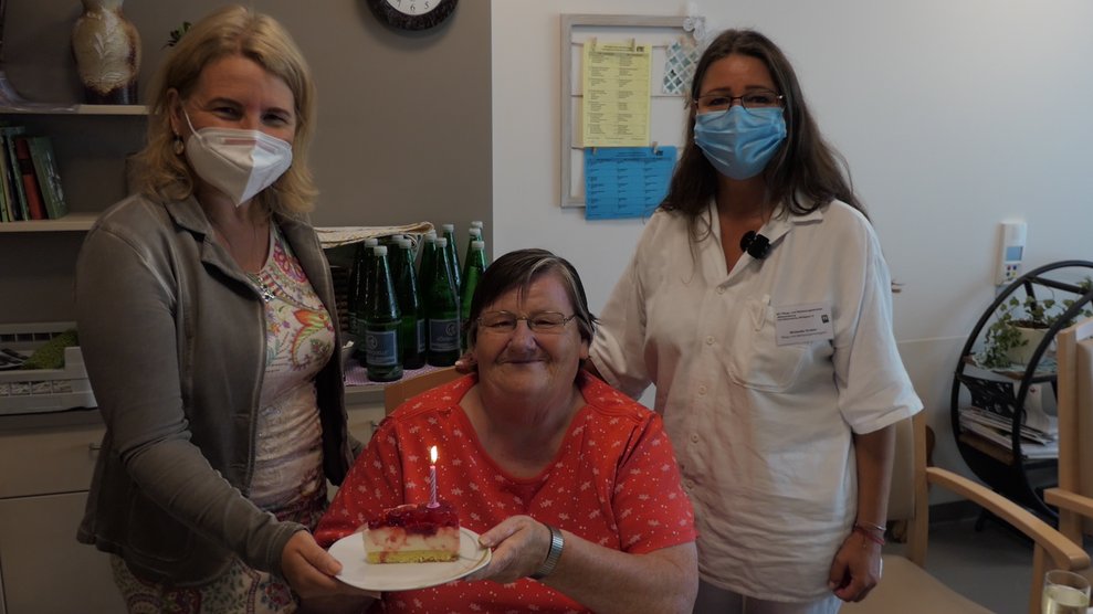 Drei Frauen mit einem Stück Torte, darauf brennt eine Kerze.