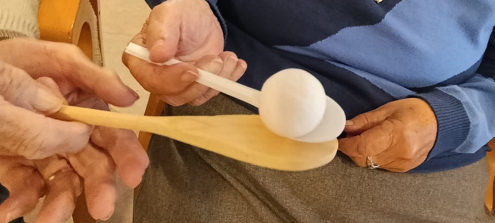 Hände halten Kochlöffeln und kleiner Ball liegt auf Kochlöffel.